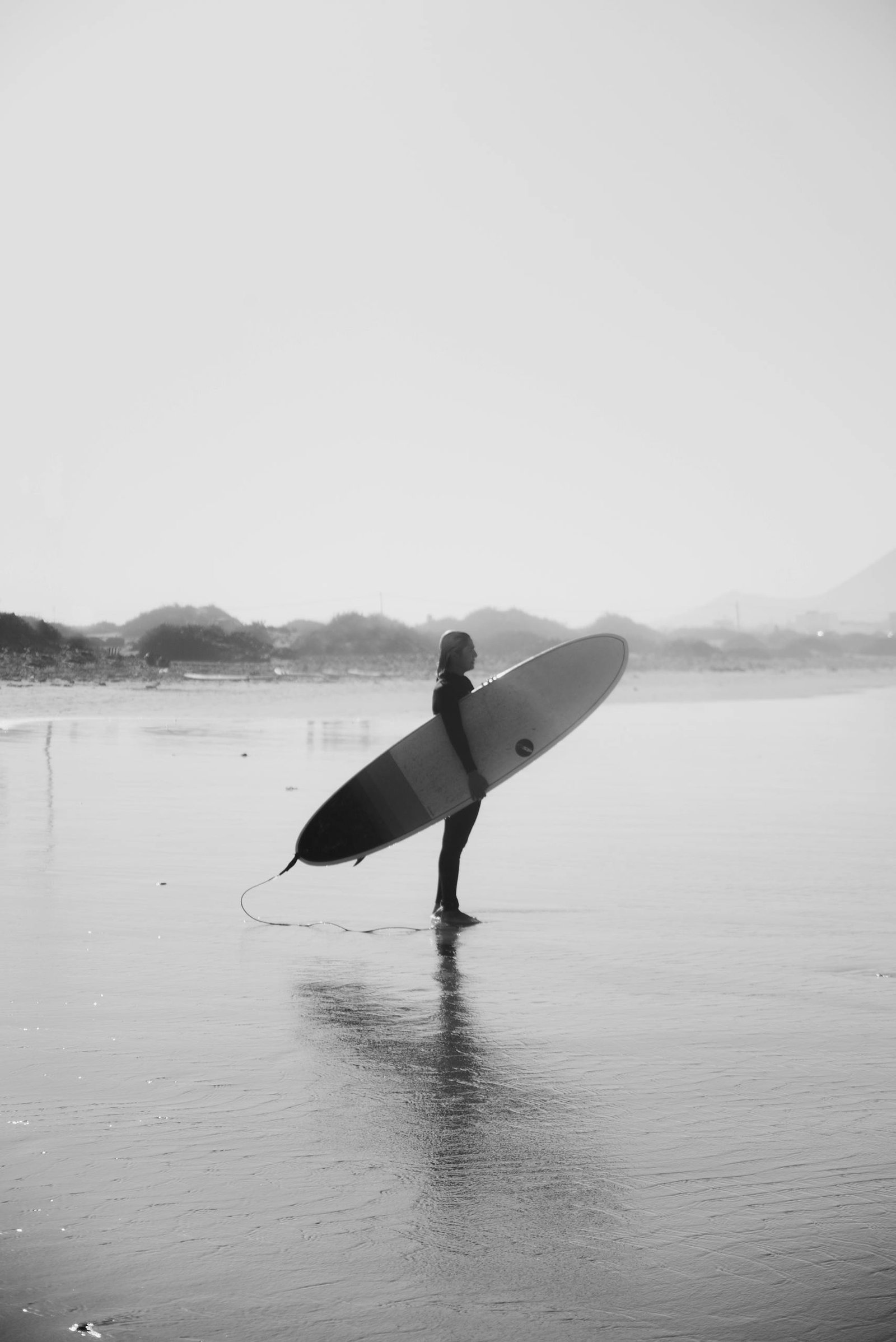 Gray-scale Photo of Man Holding Surfboard Standing on Beach