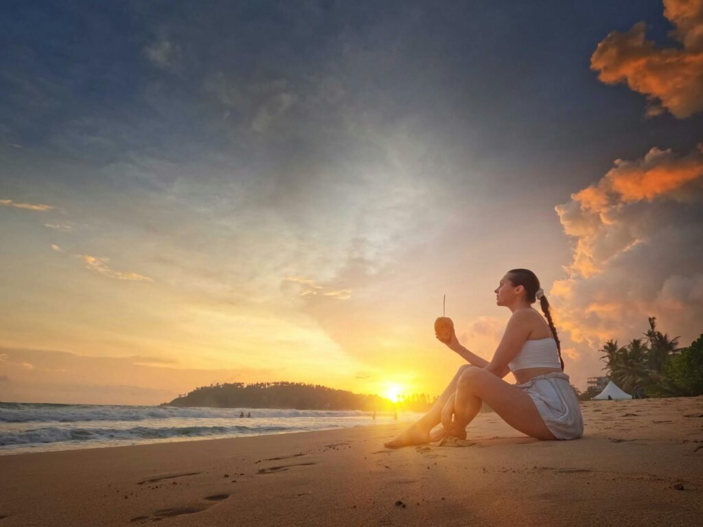 woman sitting on the shore of the beach while holding a glass