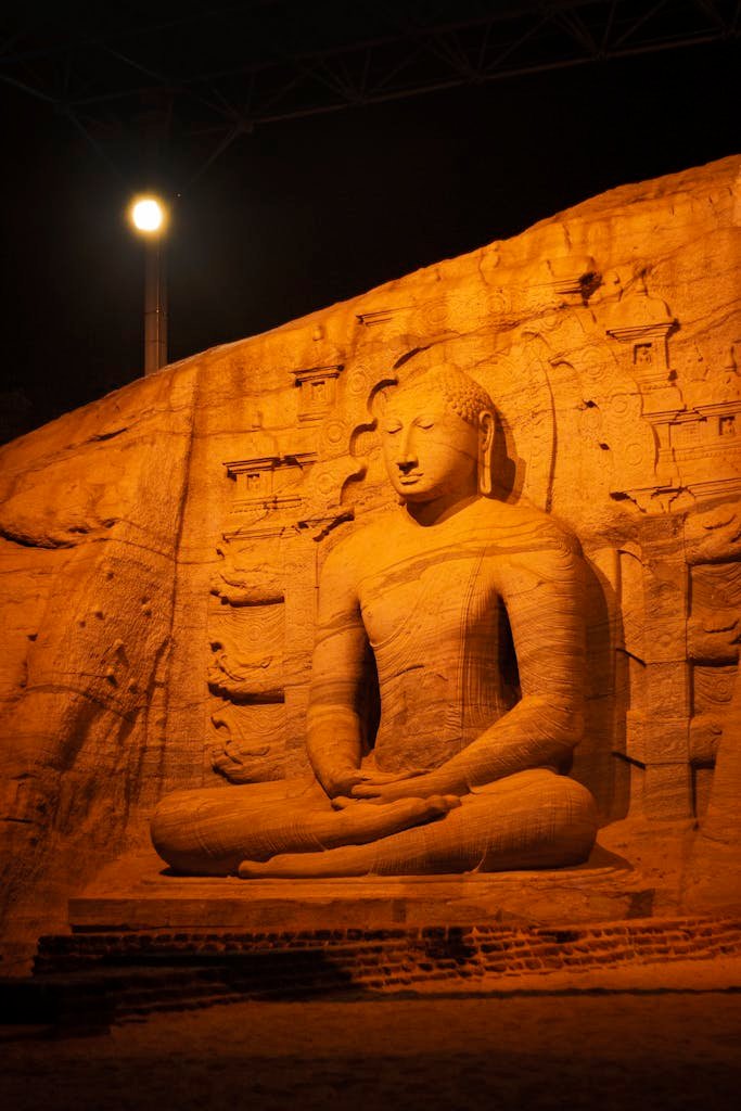 Illuminated Buddha statue in Polonnaruwa, Sri Lanka under night sky, showcasing religious significance.