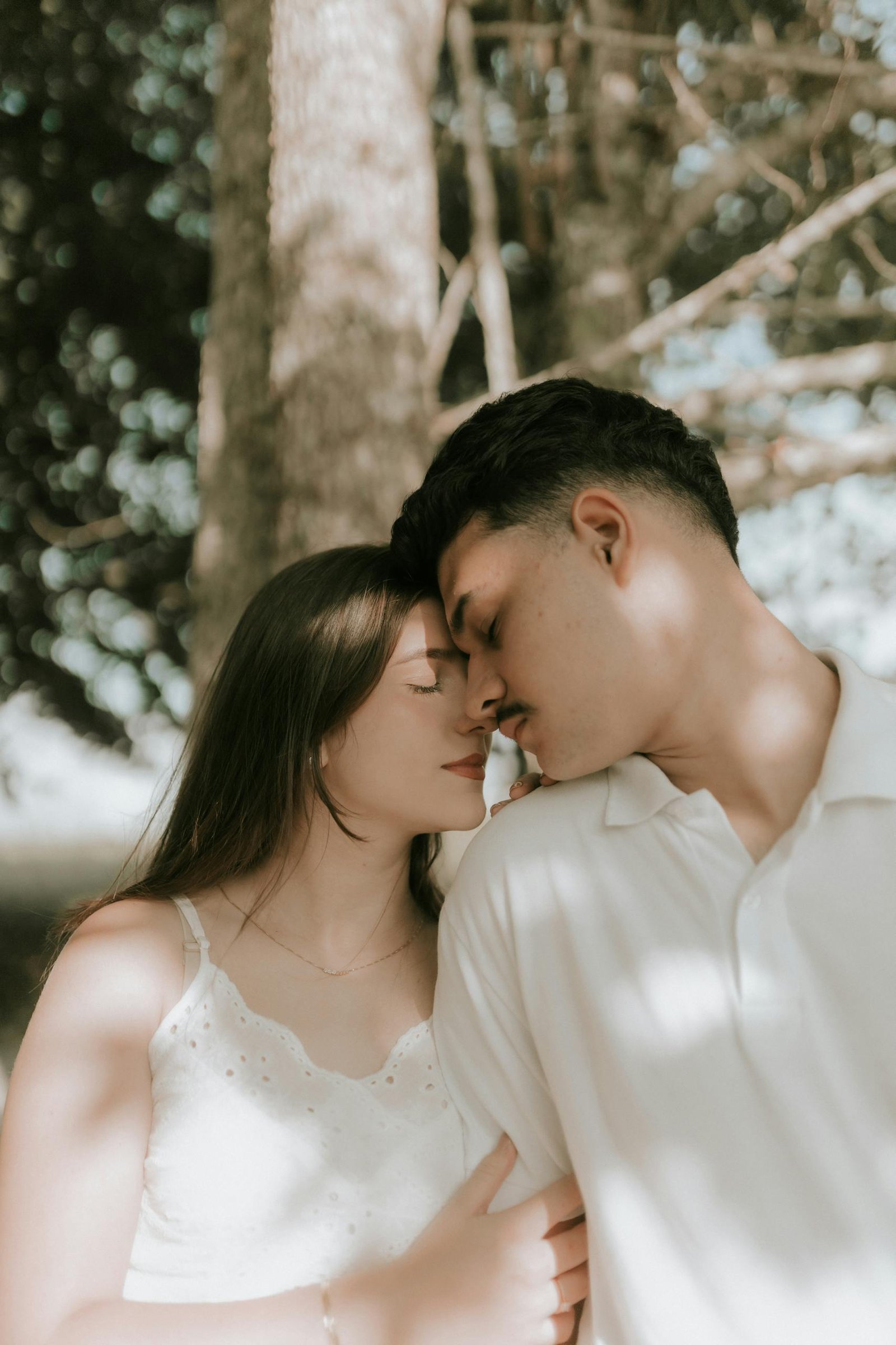 Tender moment of a couple embracing outdoors under the soft shade of a tree.